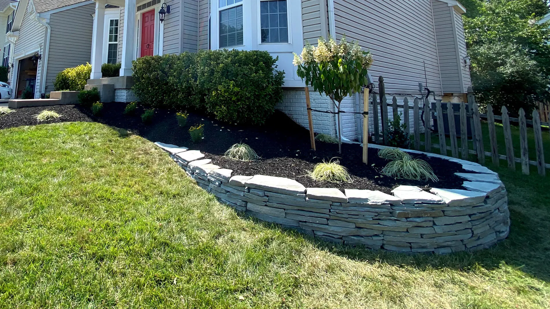 Front landscape in Bristow, VA, with a stone retaining wall and plants.